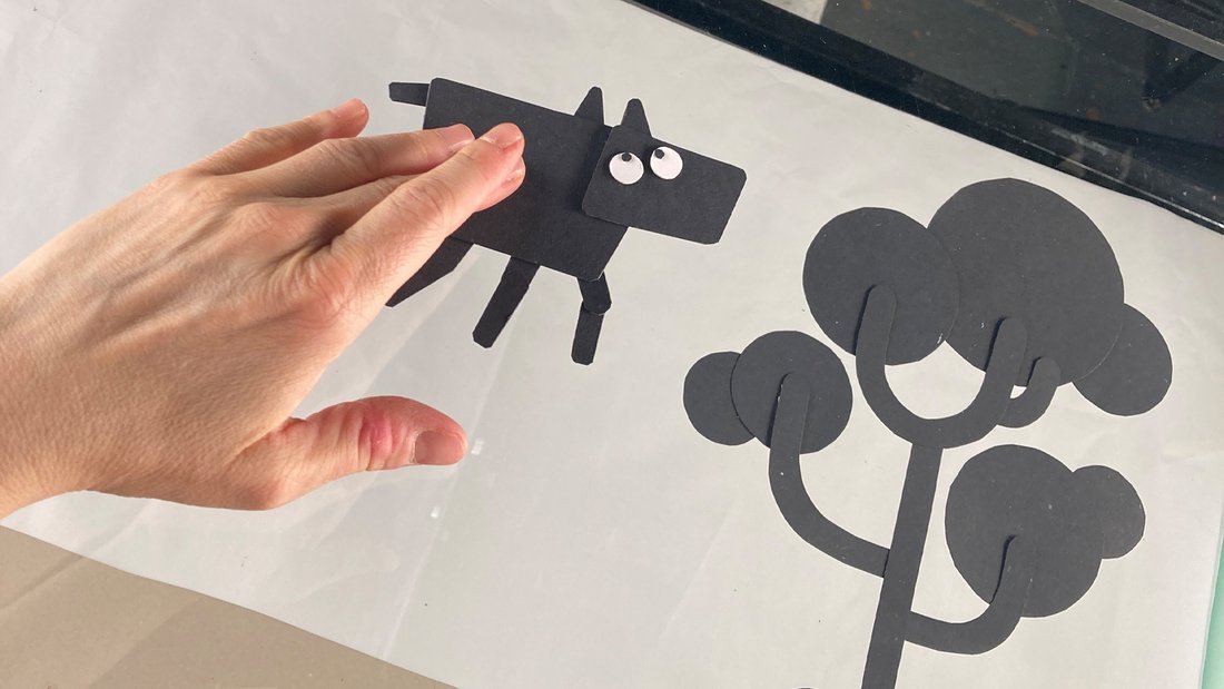 A dog made of black cardboard touched by a hand.