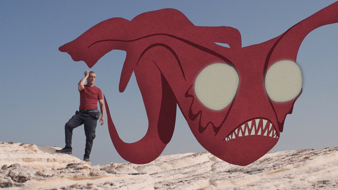 Ship Of Fools - Still - A man standing on rocks with a scary dragon like red animal flying away in front of him.