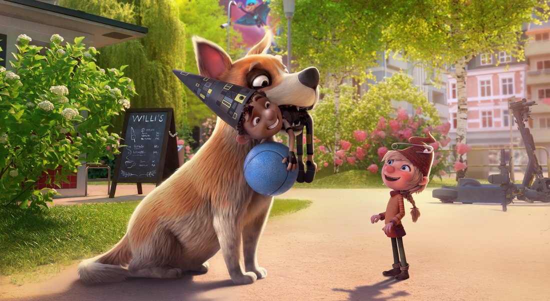 Dog playfully holds boy while girl laughs in sunny park.