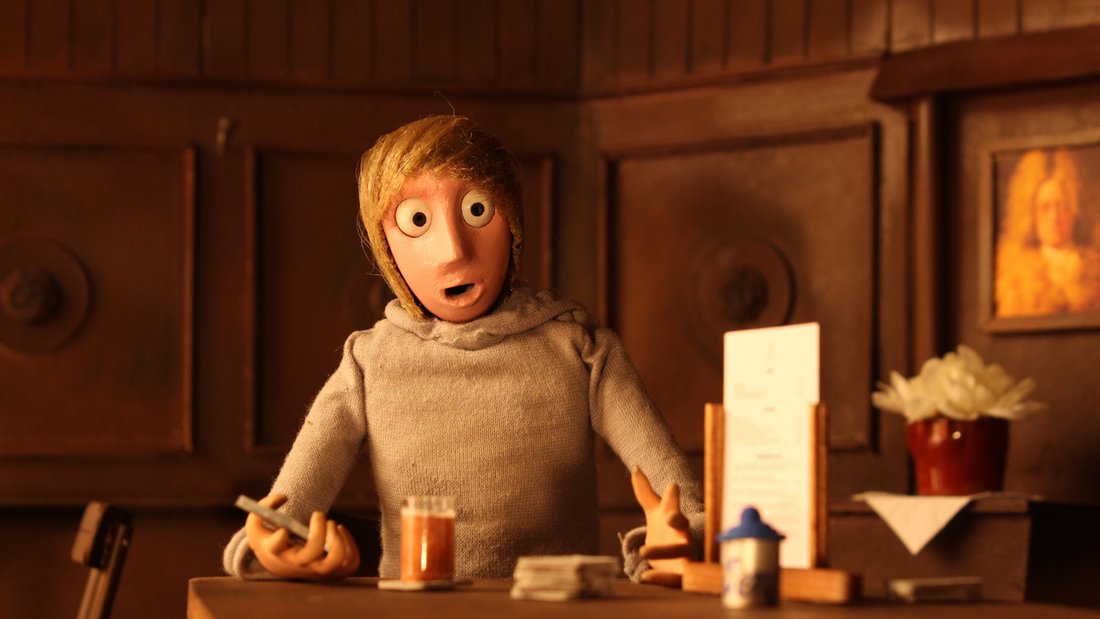 Time App - Still - A boy in a old time bar, staring surprised into the camera with a smartphone in his right hand.