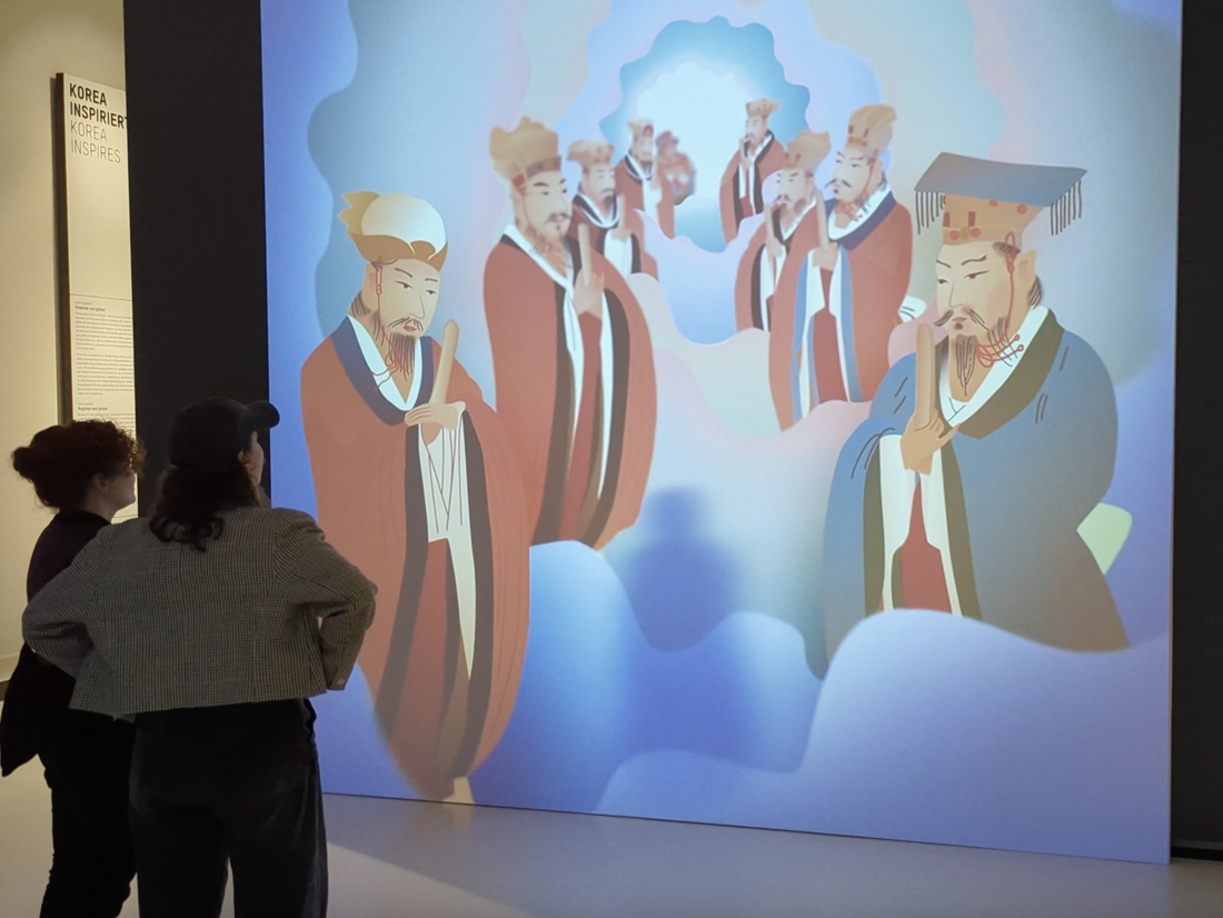 Jijang Siwangdo - Still - Two woman looking at an animated museum exhibition installation depicting a group of Korean buddhist monks on clouds.