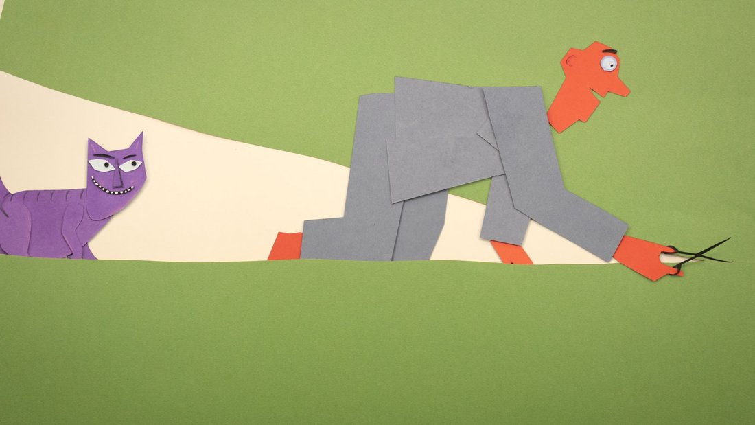 A man crawling cuts up a sheet of paper, followed by a cat