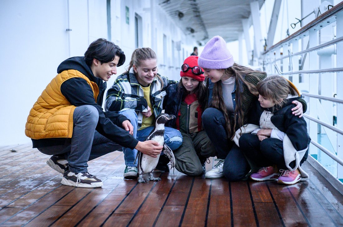 Chaos Sisters - Still - A group of young friends on a ship, petting a penguin amidst them.